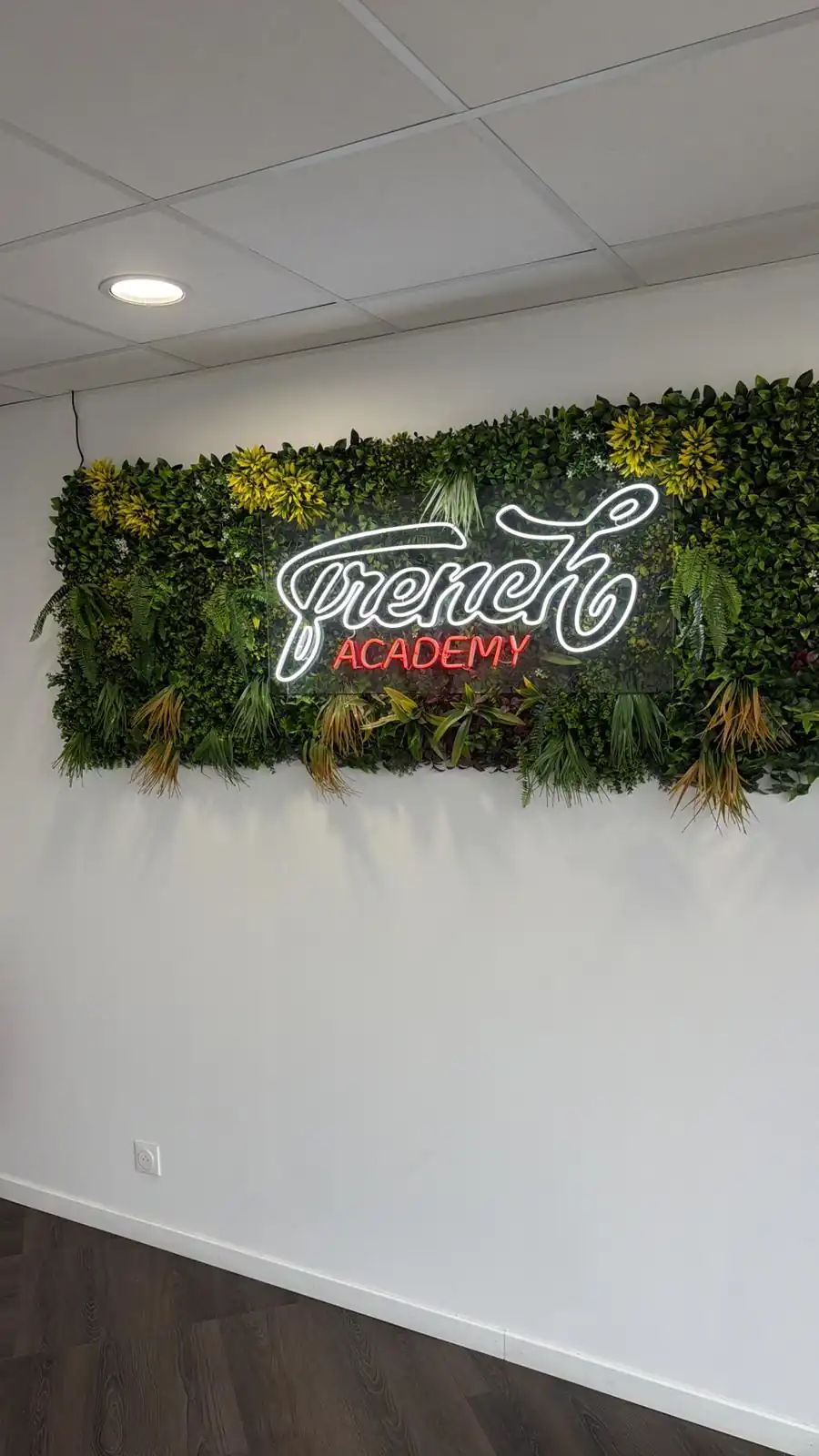 Enseigne néon French Academy sur mur végétal